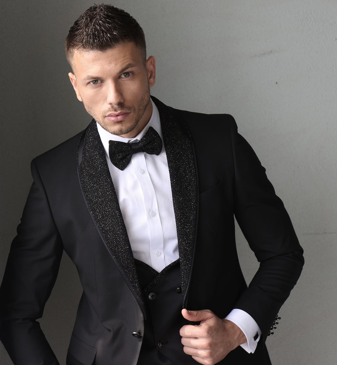 Man wearing a black and gold glitter lapel tuxedo with a matching bowtie and vest.